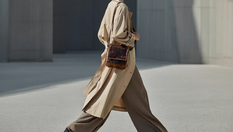 Woman walking with a brown leather crossbody bag in an urban minimal setting